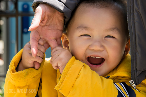 Here's an example of directly engaging my subject. In this case the little boy found me and my camera humorous and entertaining yet didn't want to leave the security of his mother, huddled between her body and arm and hanging on to her hand. This photo is all about gesture and the pure joy of this little boy